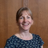 Photograph of a white female in her late forties with long blonde hair. She is smiling and wearing a navy top.